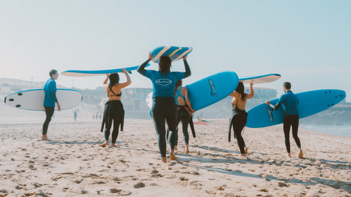 Group of surf students walking in the beach while holding their surfboards